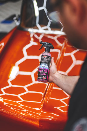 A person holding a bottle of P and S Dream Maker in front of an orange vintage car.