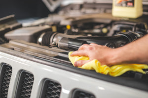 A person cleaning under the hood of a car with a yellow towel.