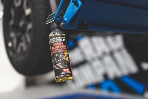 A spray bottle of P and S Iron Buster hanging from a blue car lift, with a blurred background showing a car tire.