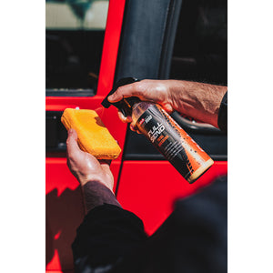 A person spraying P and S Full Send on a yellow sponge in front of a red jeep.