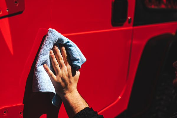 A person wiping a red jeep with a Rag Company towel.