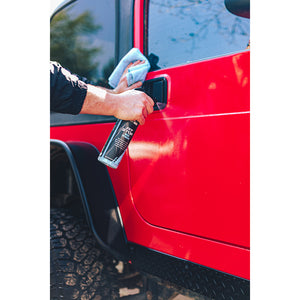 A person spraying P and S Pit stop on the car door of a red jeep .