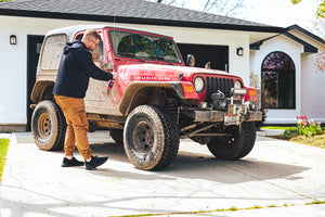 A person spraying P and S Mud Buster on their muddy red jeep.