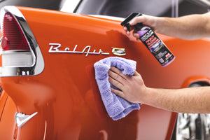 A person cleaning an orange car with P and S Paint gloss and a lavender towel.