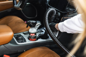 P&S Release bottle in the cupholder of a jeep next to a person vacuuming out the cupholder next to it.
