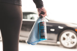 A close up of a person holding a blue rag and P and S True Vue with a blurry background of a car.