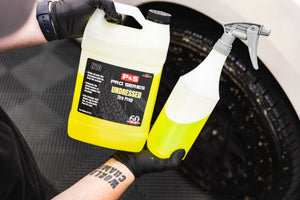 A Jug and spray bottle of P&S Undressed held by a person with gloves against a car tire background.