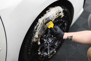 Person cleaning a car tire with a Detail Factory Wheel Brush with P&S Undressed.