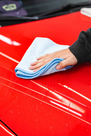 Person cleaning a red car with a blue ftw microfiber towel