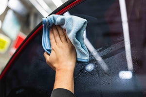Person cleaning a car window with a blue FTW microfiber.