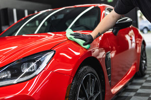 Person cleaning a red car with a green FTW microfiber towel.