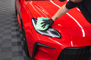 Person cleaning a car front headlight with a green FTW microfiber.