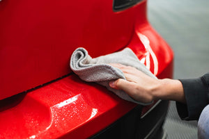 Person cleaning a car bumper with an ice grey FTW microfiber.