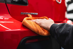 Person cleaning a car bumper with an orange FTW microfiber.