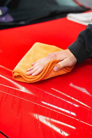 Person cleaning the hood of a red car with a orange FTW microfiber towel.