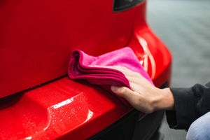 Person cleaning a car bumper with a pink FTW microfiber.