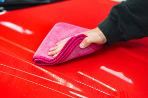 Person cleaning a car hood with a pink FTW microfiber.