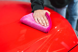 Person cleaning a car hood with a pink FTW microfiber.