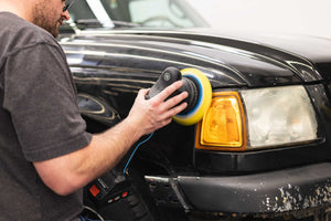 A person using a rupes da yellow pad on a rupes polisher on a black truck.