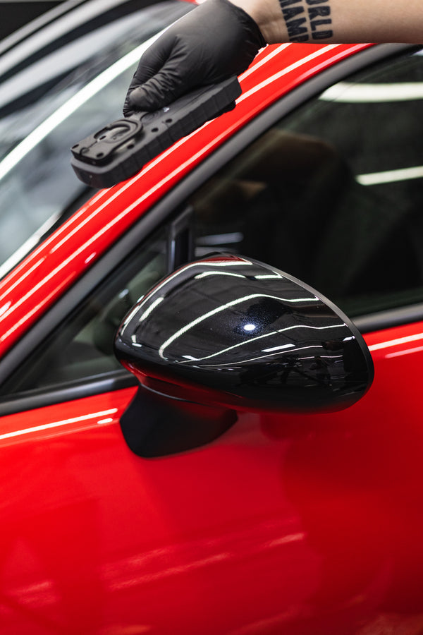 Person wearing black gloves using a scangrip light on a car mirror on a red vehicle