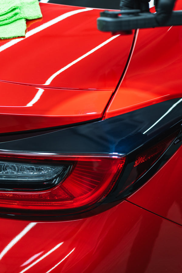 Close-up of a red car with a black accent being cleaned.
