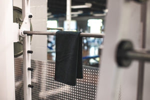 The Rag Company Spa and Workout 16x27 black towel hanging on a metal workout bar.