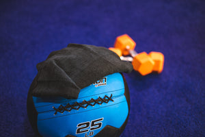 The Rag Company Spa and Workout 16x27 black towel laying on top of a blue ball.