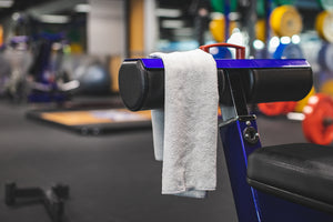The Rag Company Spa and Workout 16x27 ice grey towel hanging on a workout machine.