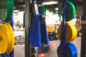 The Rag Company Spa and Workout 16x27 royal blue towel hanging on a squat rack.