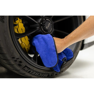 A person cleaning tire rims of a car with a blue spectrum towel.