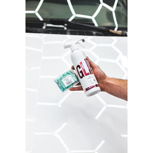 A hand holding a bottle of Stjarnagloss Clay Lubricant and the Lera Clay Bar over a white car hood.