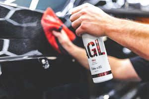 A person spraying Parla onto a black car while wiping it with a red rag.