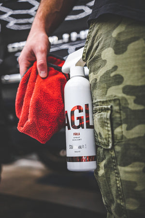 Close-up of a person in camouflage pants holding a red microfiber towel and a bottle of Parla Spray Sealant.