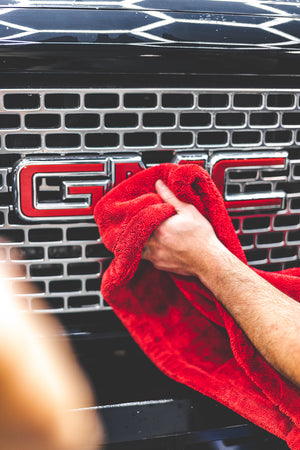 A hand cleaning the GMC logo on the front of a truck with a Red 1500 towel.