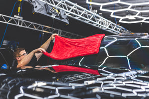 A person fanning a red 1500 towel over the front window of a black truck.