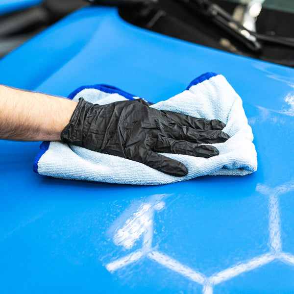 A hand wearing a black glove wiping a blue Subaru Crosstrek with a blue Premium FTW Towel.