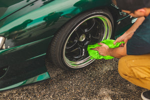 A person drying the tire of a green car with a lime green towel.