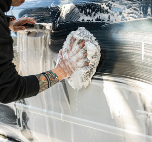 A person scrubbing the side of a grey car covered in foam with a grey Cyclone rag.