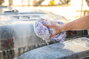 A person scrubbing the hood of a jeep covered in foam with a purple Cyclone rag.