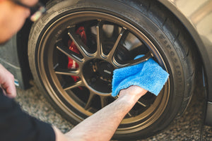 A person cleaning the tire rims of a car with a blue eaglet towel.