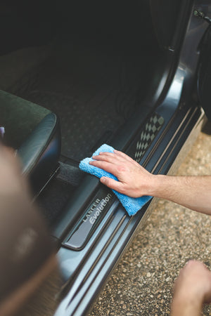 A person cleaning the edge of a car door with a blue Eaglet towel.