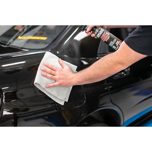 A person wiping the back of a black vehicle with a grey edgeless towel.