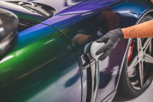 A person scrubbing the handle of a car with a pearl puck applicator.