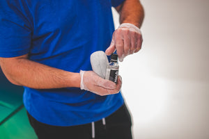 A person holding a gray puck applicator and Gtechniq Halo with a white background.