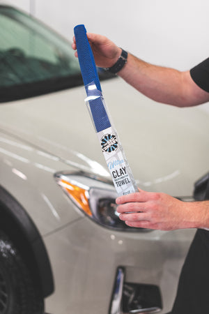 A person taking an Ultra Clay Towel out of its packaging and in front of a car.