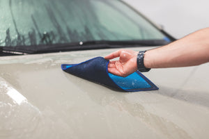 A wet hand flipping over a blue Ultra clay towel on the hood of a car.