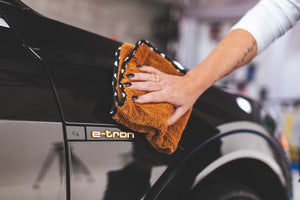 A person drying the side of a black car with a rust colored Wolfpack towel.