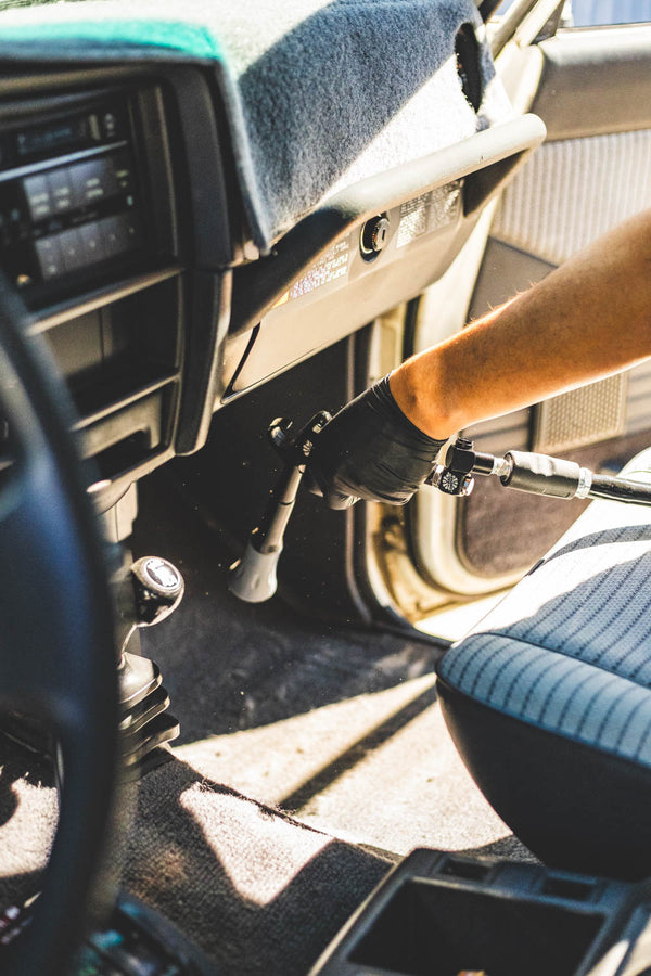 A closeup of a person using the Ultra Air Blaster to clean the floor of a car.