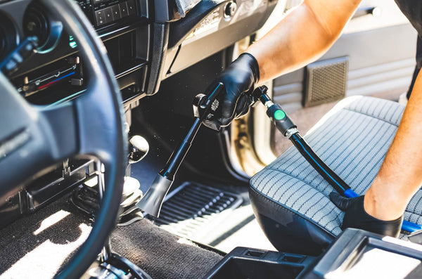 A closeup of a person using the Ultra Air Blaster to clean the floor of a car.