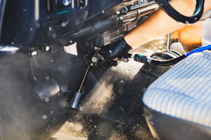 A closeup of a person using the Ultra Air Blaster to clean the floor of a car.